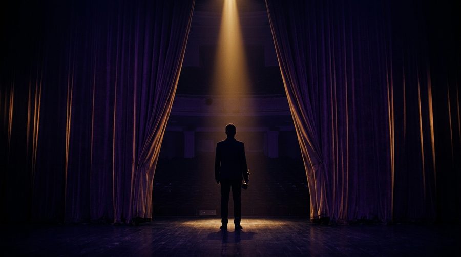 Siluet pemenang berdiri di balik tirai teater yang sedikit terbuka dengan sorot cahaya keemasan